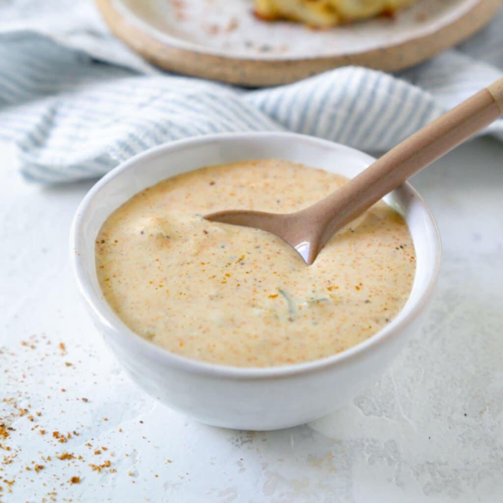 A white bowl filled with crab cake sauce on top a white counter.