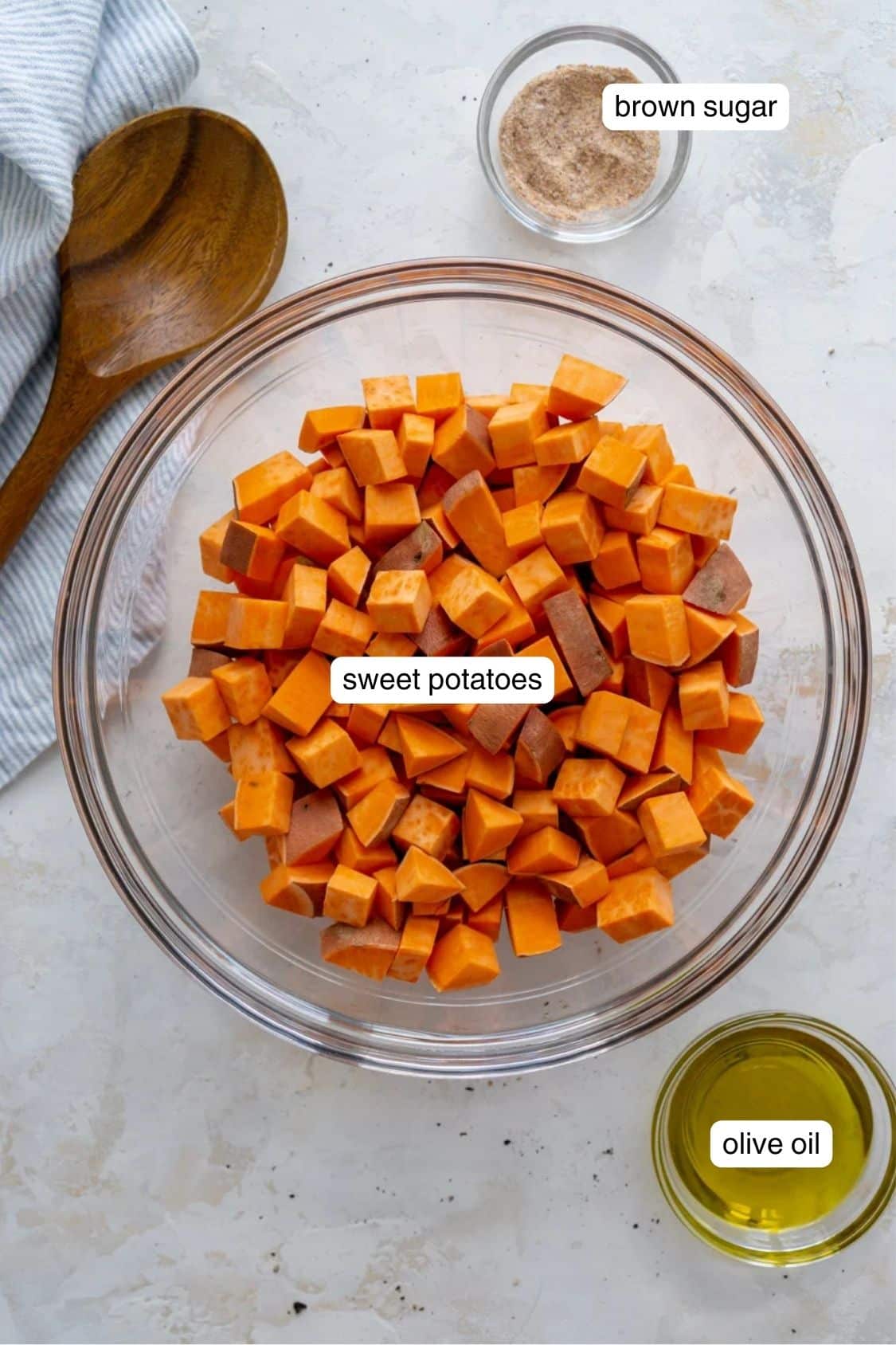 Cubed sweet potatoes in a bowl next to olive oil and a bowl of brown sugar.