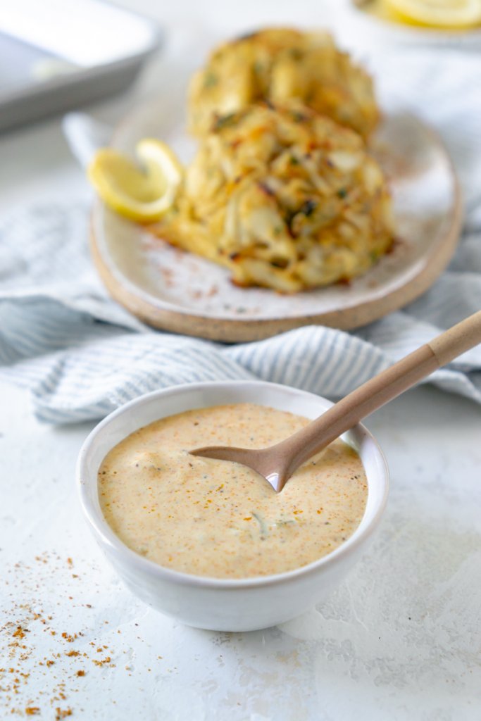 sauce in a small white bowl, crab cakes in background