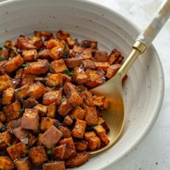 roasted sweet potatoes in a white bowl with gold spoon