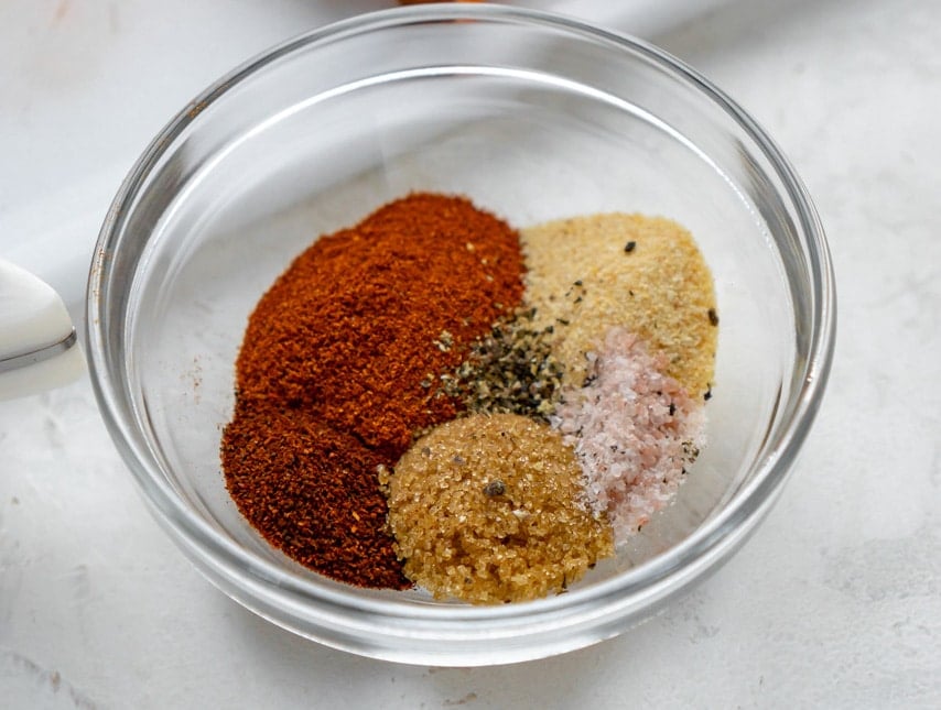 Salt, pepper, brown sugar, chili powder, paprika, and garlic powder in a glass bowl.