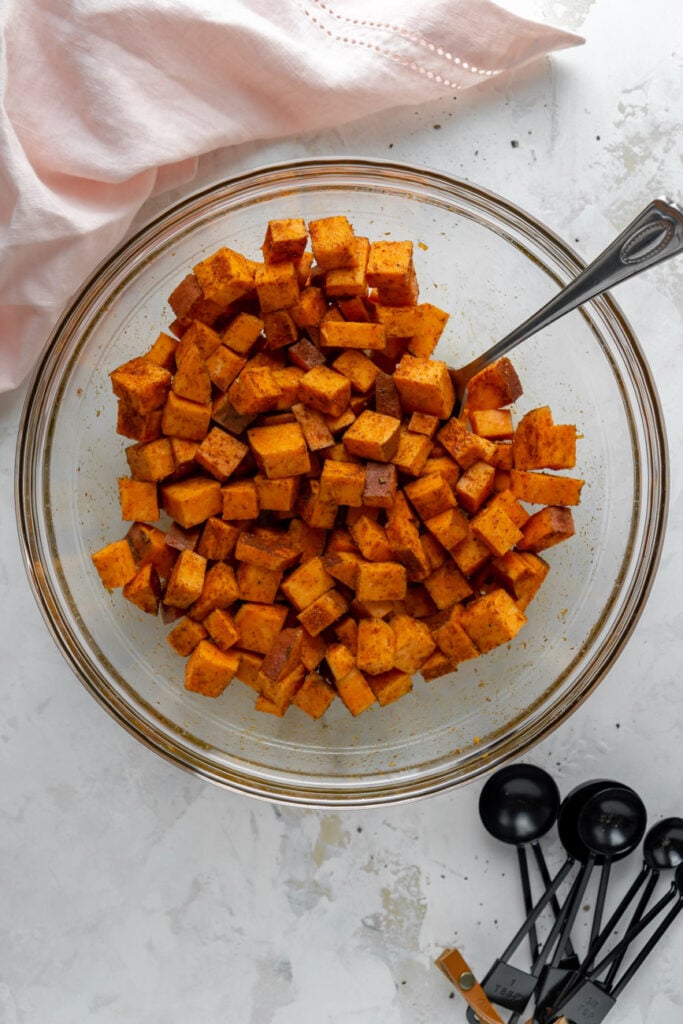 Sweet potatoes in a glass bowl tossed with oil and seasonings.