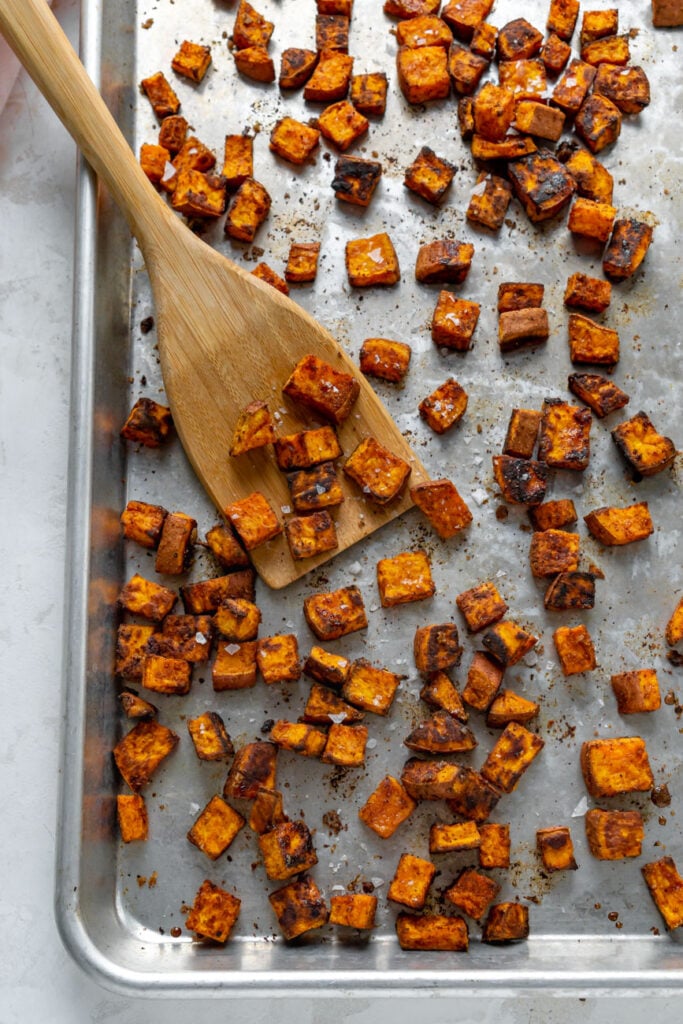 Roasted sweet potatoes on a sheet pan with a wooden spoon.