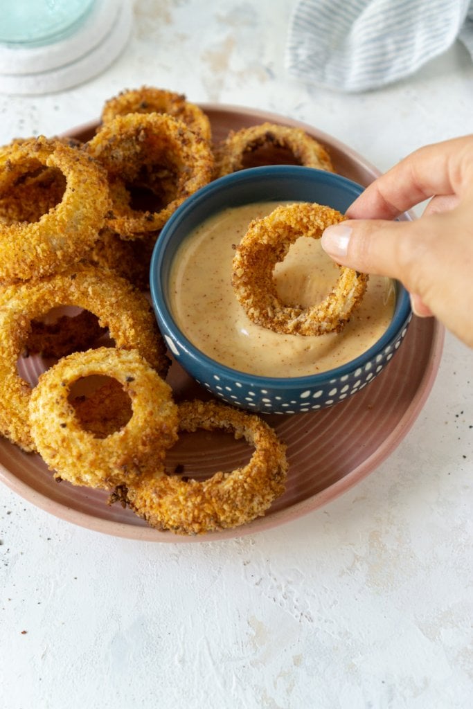 hand dipping an air fryer onion ring in sauce