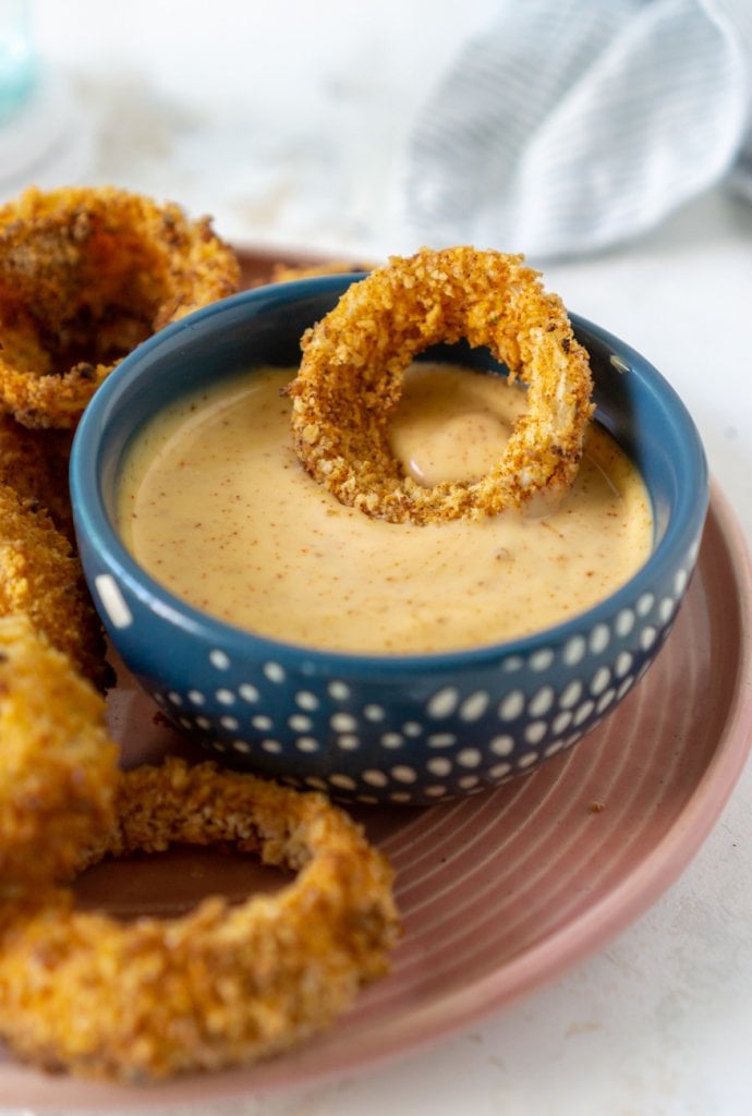 air fryer onion rings on a plate, one in sauce