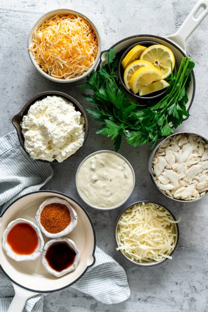 ingredients in small bowls: shredded cheese, lemons, cream cheese, tartar sauce, lump crab