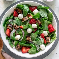 strawberry caprese chicken salad in a large white bowl with dressing to the side