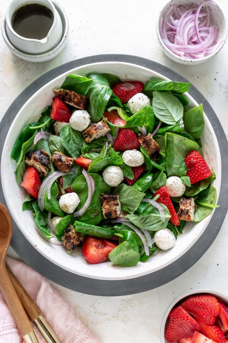 strawberry caprese chicken salad in a large white bowl with dressing to the side