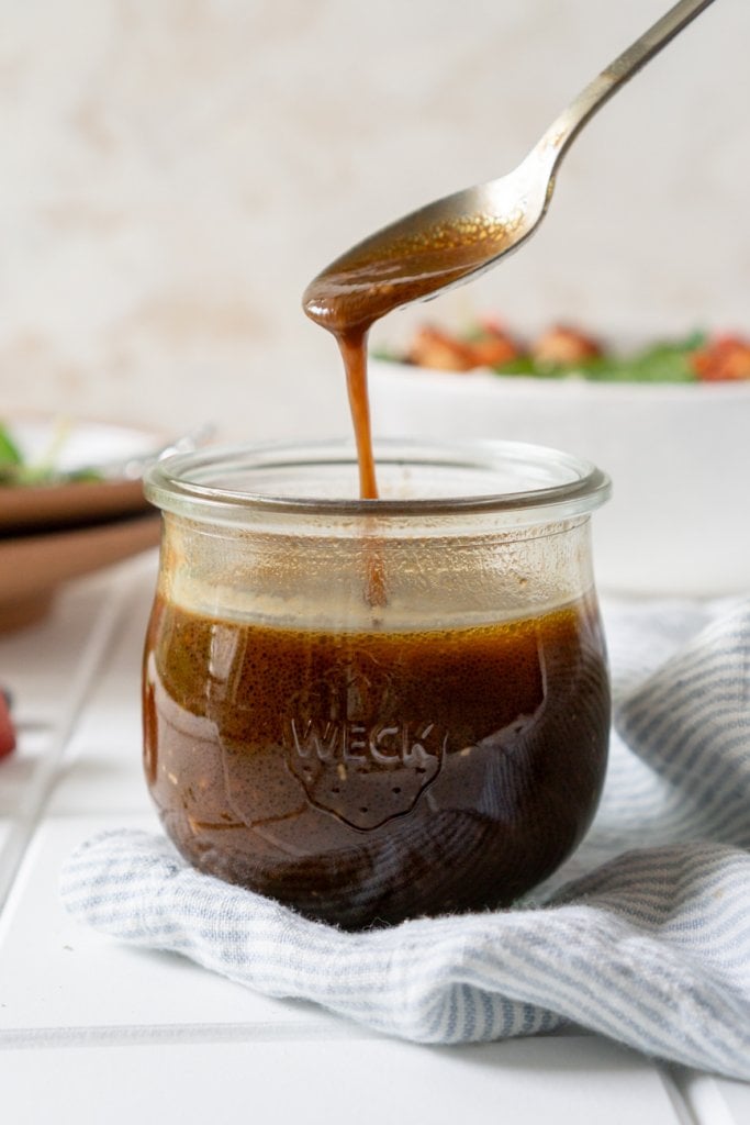 balsamic dressing dripping off a spoon into a glass jar