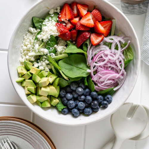 spinach, strawberries, avocado, red onion, blueberries, goat cheese in a salad bowl