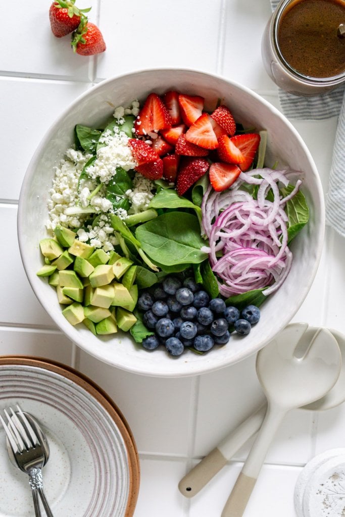spinach, strawberries, avocado, red onion, blueberries, goat cheese in a salad bowl