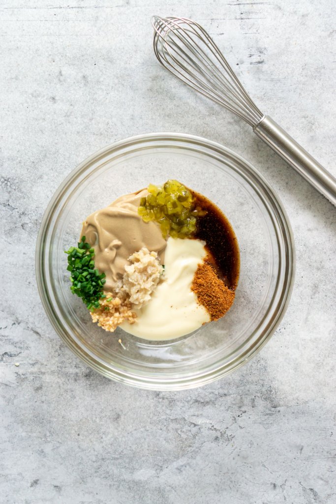 remoulade sauce ingredients in a glass mixing bowl with a whisk