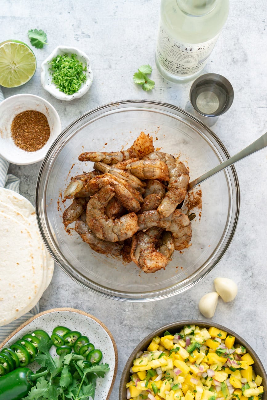 Seasoned shrimp in a glass bowl with a spoon.