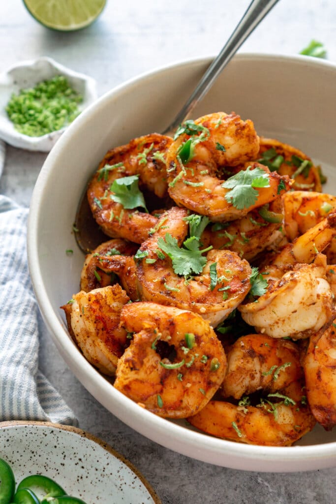 Tequila lime shrimp, garnished with cilantro, in a white bowl with a spoon.