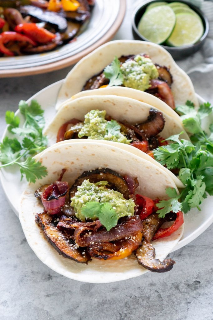 3 mushroom fajitas tacos on a plate with lime wedges