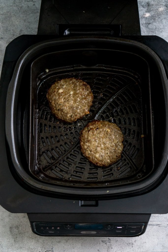two frozen burger patties in air fryer basket
