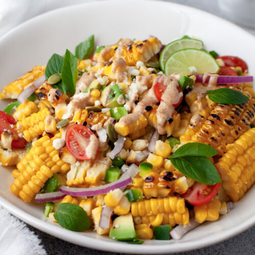 corn salad in a white bowl topped with cilantro and lime wedges