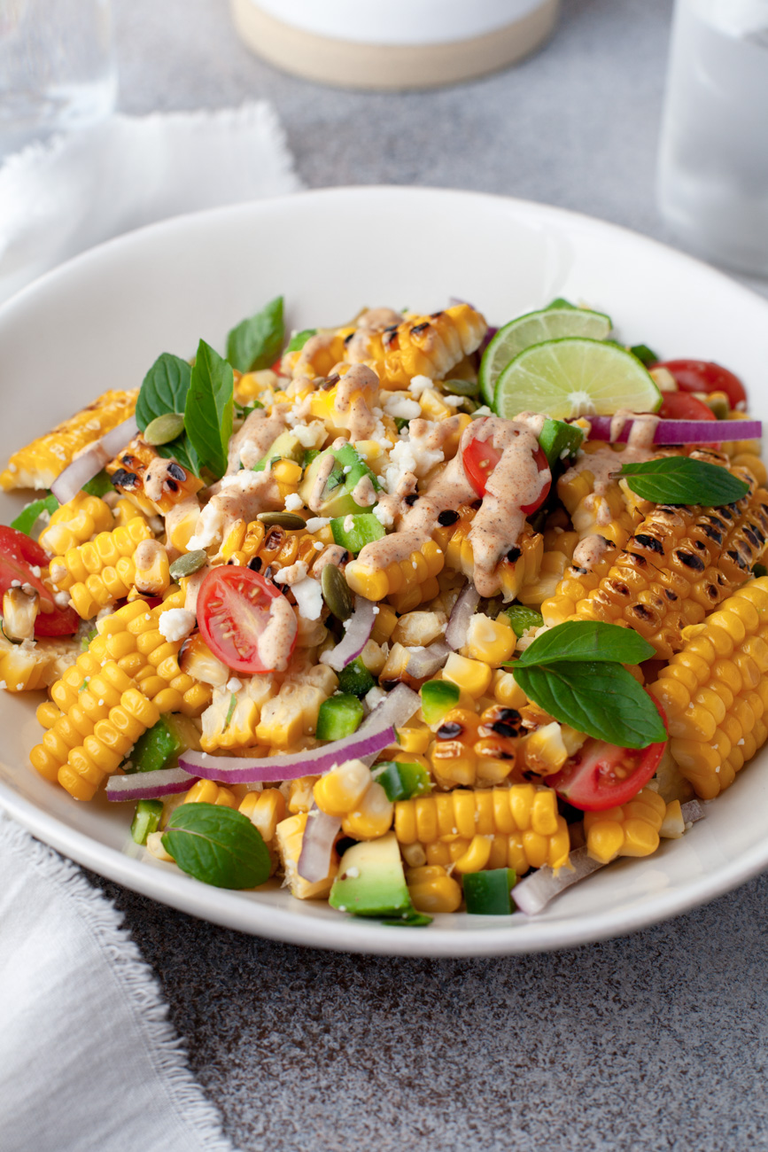 corn salad in a white bowl topped with cilantro and lime wedges