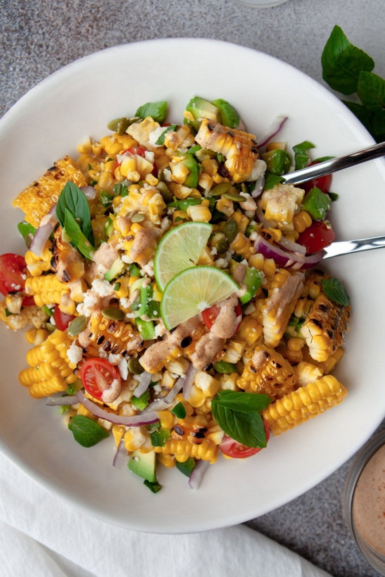 avocado corn salad in a white bowl with lime wedges