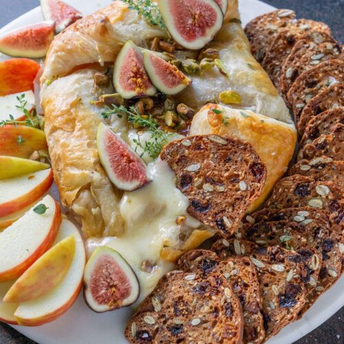 baked brie on a white tray with figs, apples, and crackers