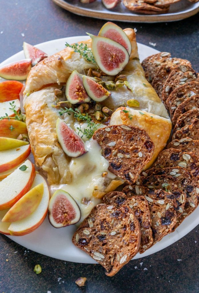 baked brie on a white tray with figs, apples, and crackers