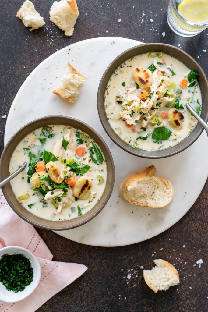 two bowls of olive garden chicken gnocchi soup with pieces of bread around