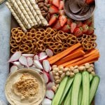 snack platter with hummus, strawberries, carrots, cucumbers, radishes, and pretzels