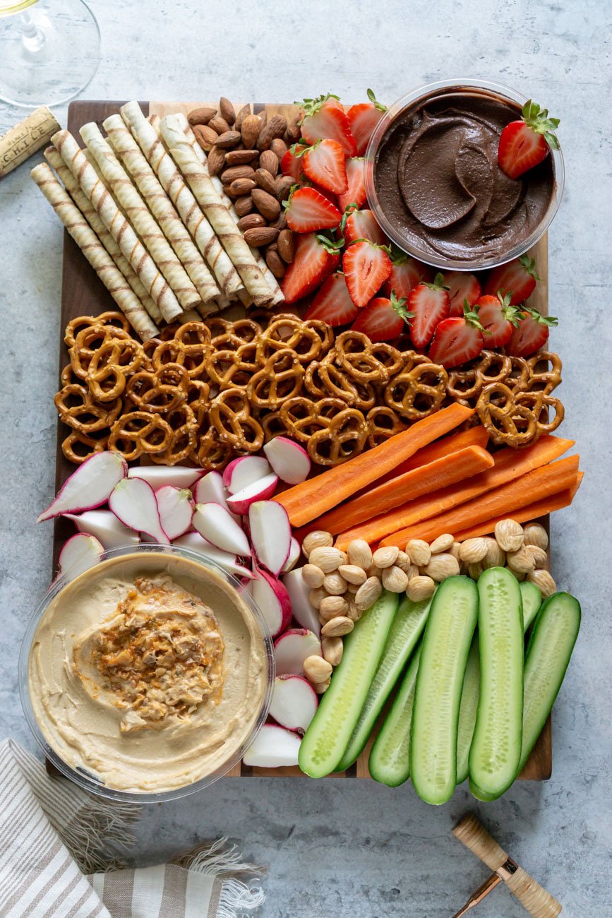 snack platter with hummus, strawberries, carrots, cucumbers, radishes, and pretzels