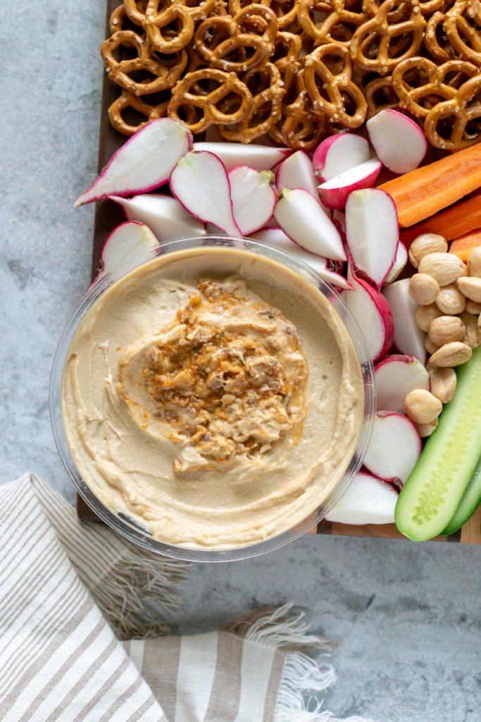 garlic hummus with radishes, pretzels, and cucumbers on a snack platter