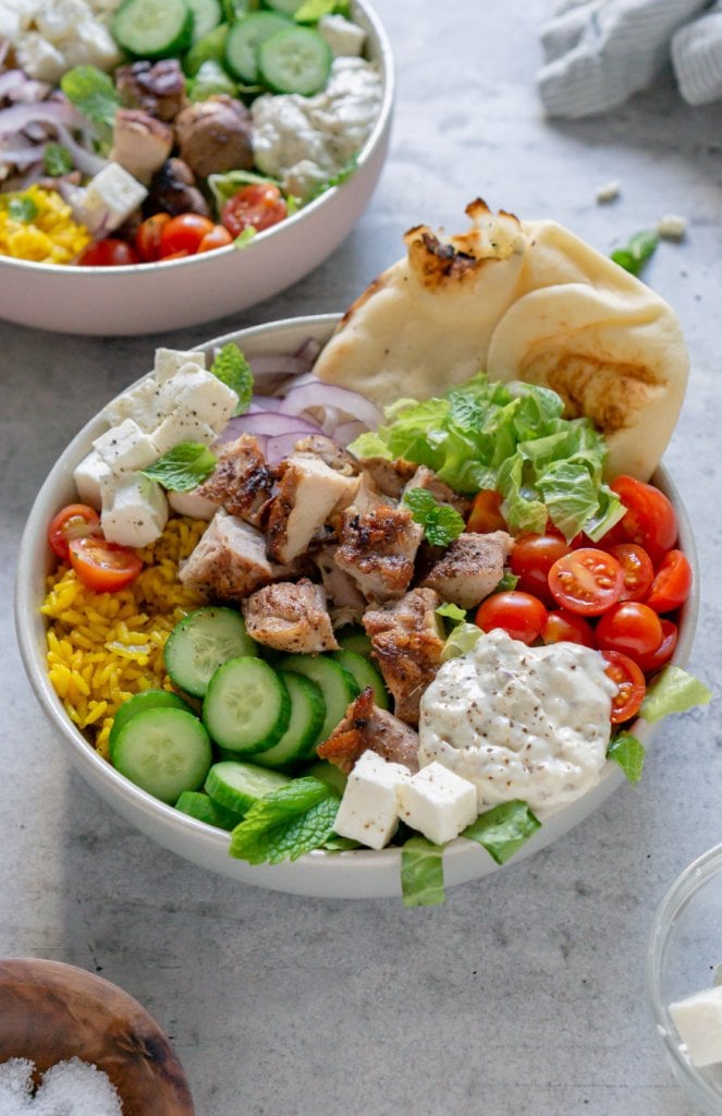 two chicken shawarma bowls with a napkin and bowl of salt