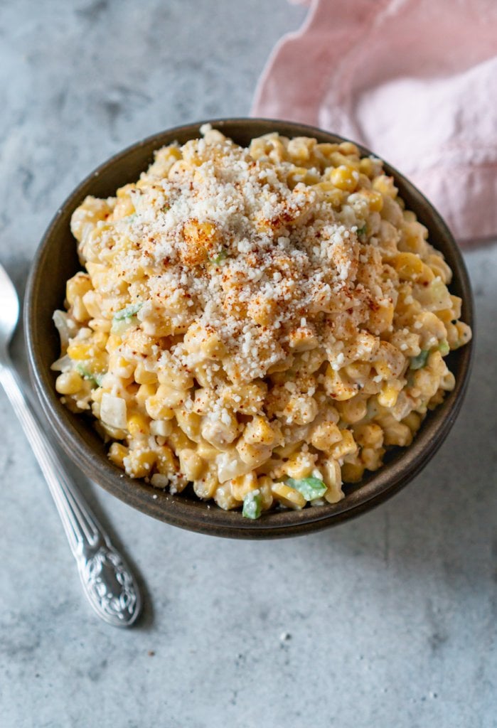 jalapeno creamed corn in a brown bowl with a silver spoon and pink napkin