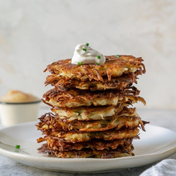 potato latkes stacked on a plate with sour cream on top