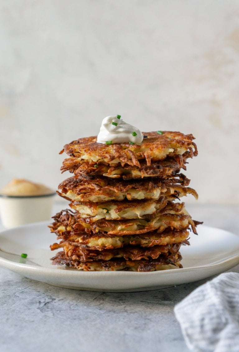 potato latkes stacked on a plate with sour cream on top