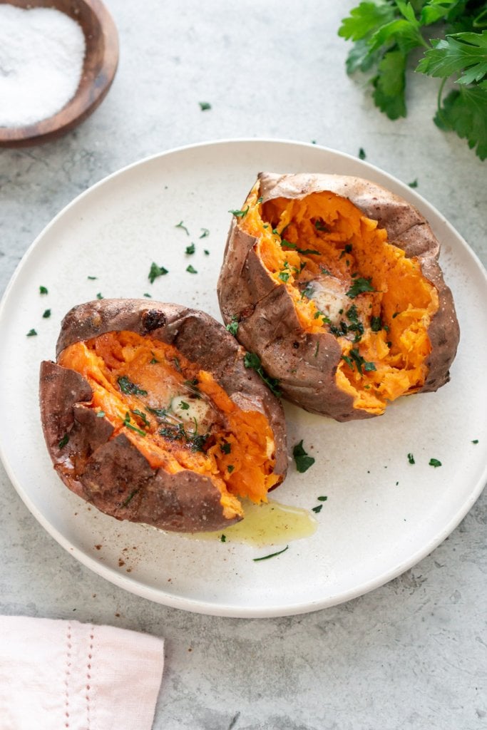 two air fryer baked sweet potatoes on a white plate with a bowl of salt and parsley to the side