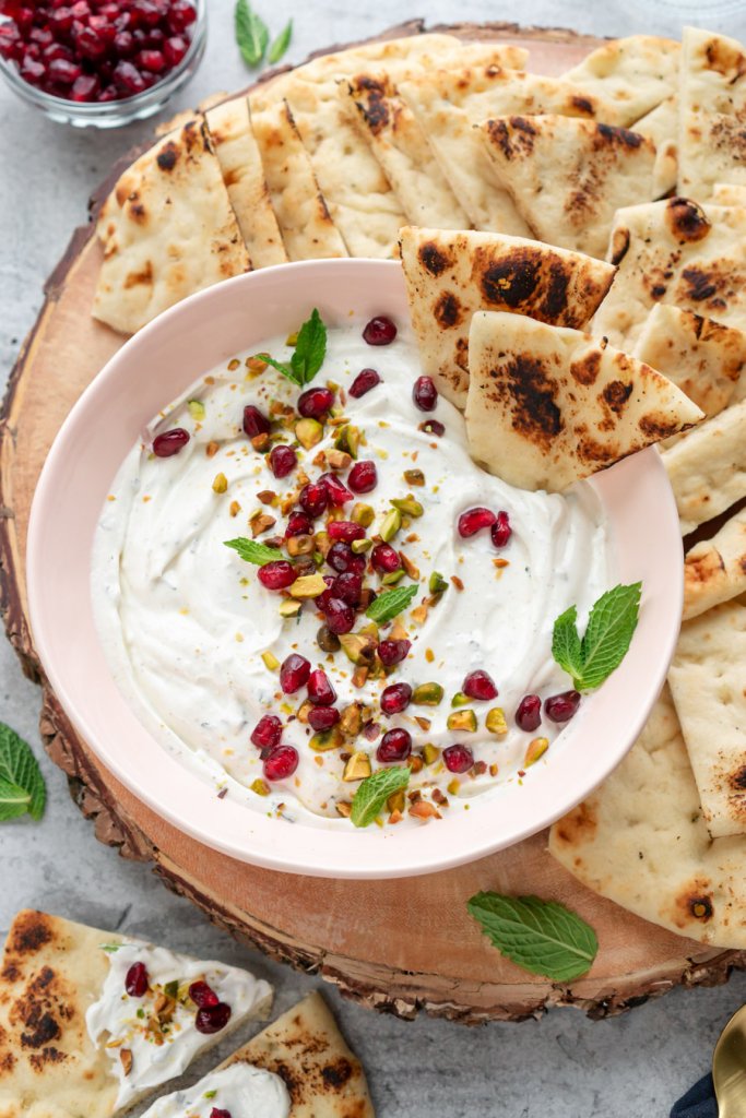 a bowl of labne dip on a wood tray with naan