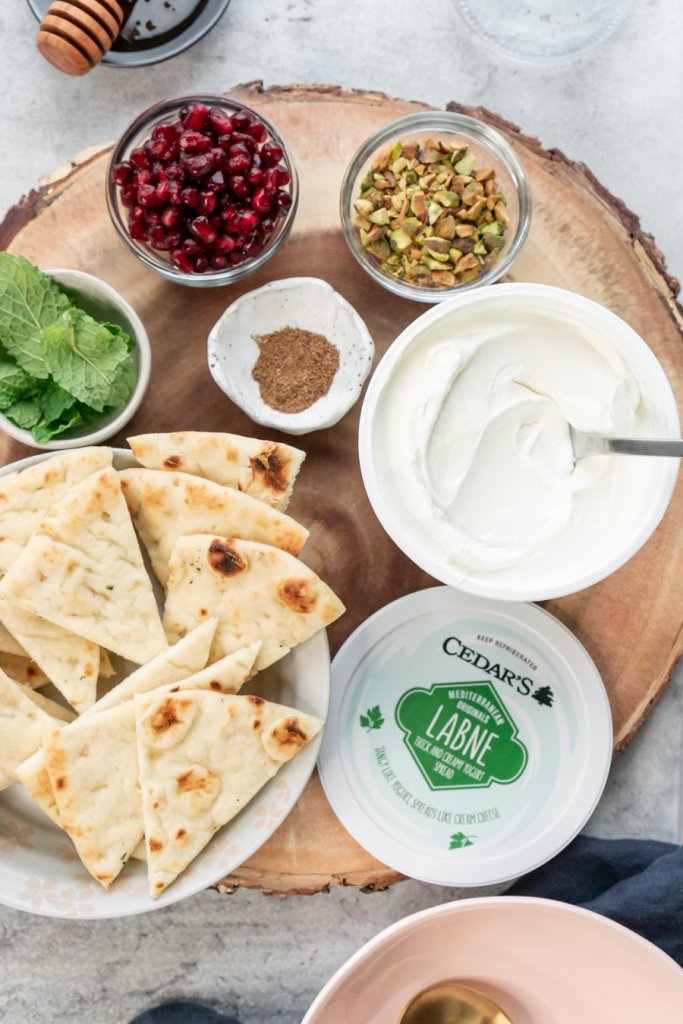 naan, labneh, pomegranate seeds, pistachios, mint, and seasoning in small bowls