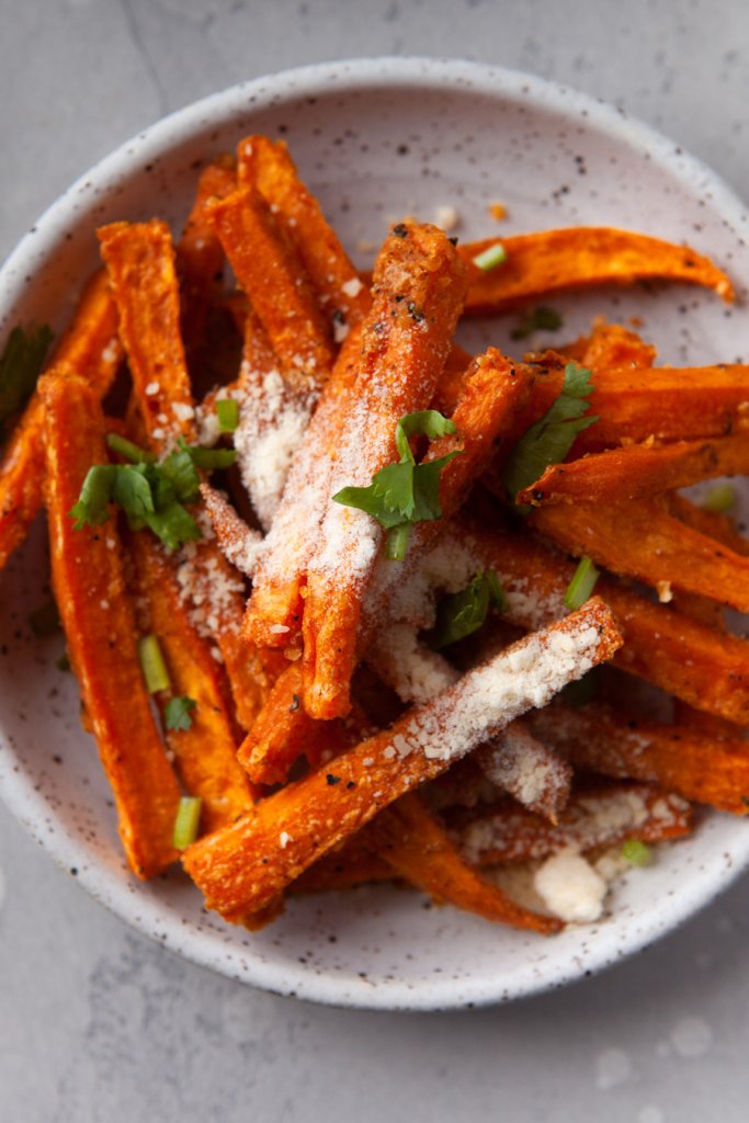 oven baked sweet potato fries on a white plate with cotija cheese and parsley