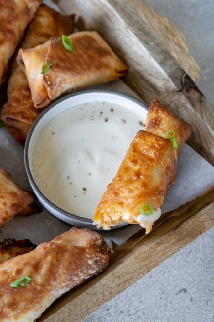 buffalo chicken egg roll with a bite taken, laying over a bowl of ranch dressing