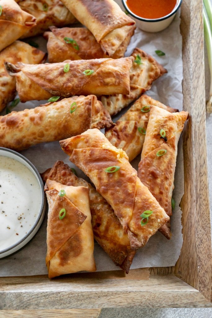 buffalo chicken egg rolls on a wood tray with ranch dipping sauce