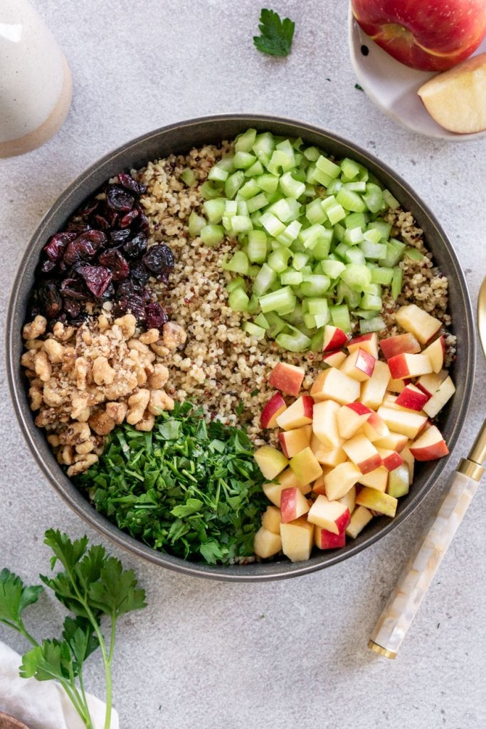 quinoa apple salad ingredients in a large dark grey bowl before being mixed