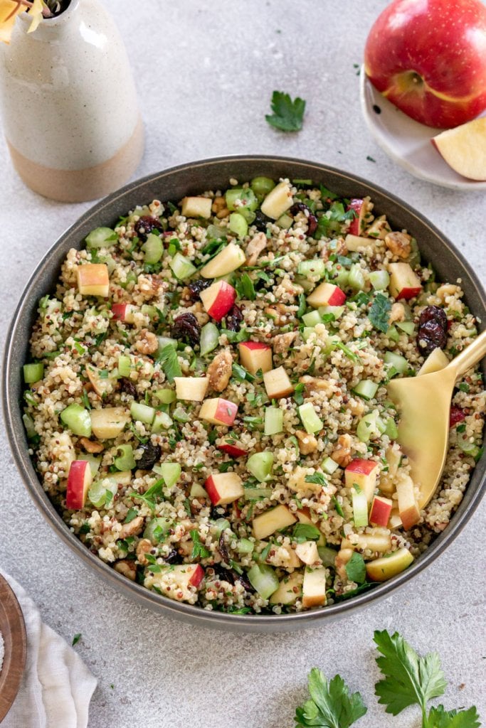 a large bowl of quinoa apple salad with a gold serving spoon and an apple to the side
