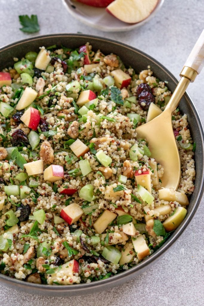 quinoa apple salad in a dark grey bowl with a gold spoon