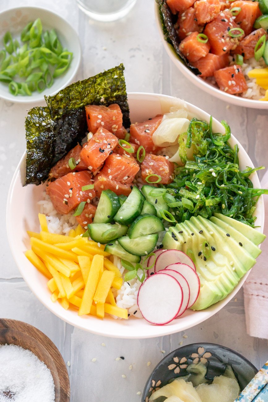 two salmon poke bowls on a light grey surface