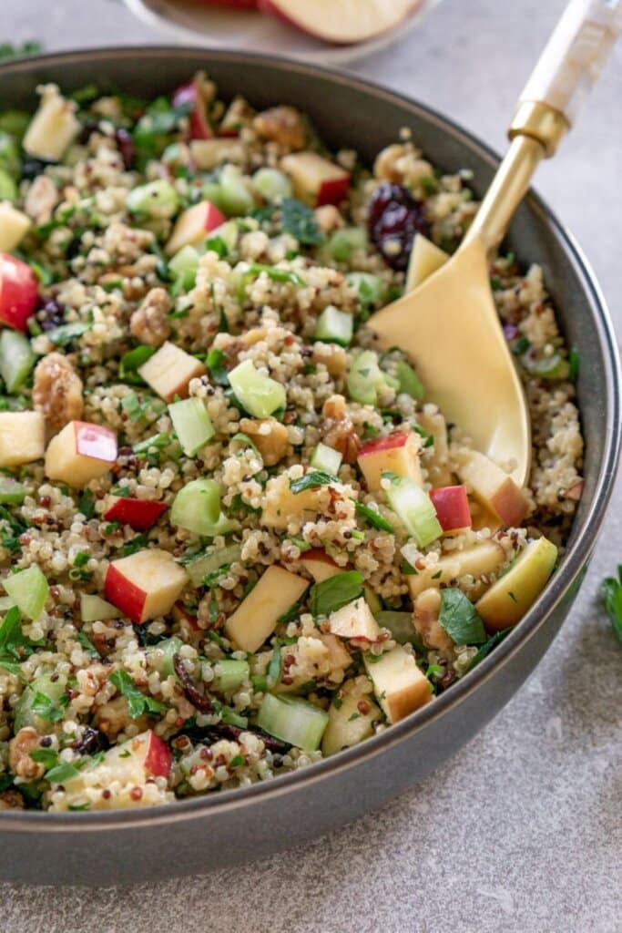 Apple quinoa salad in a gray bowl with a gold spoon.