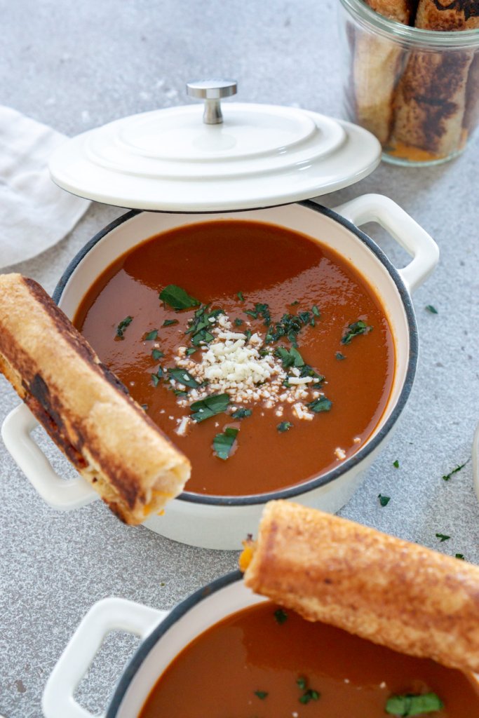 tomato soup in a white bowl with grilled cheese roll ups