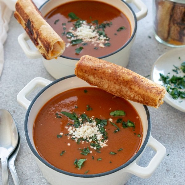 two bowls of tomato soup with grilled cheese roll ups on the edge