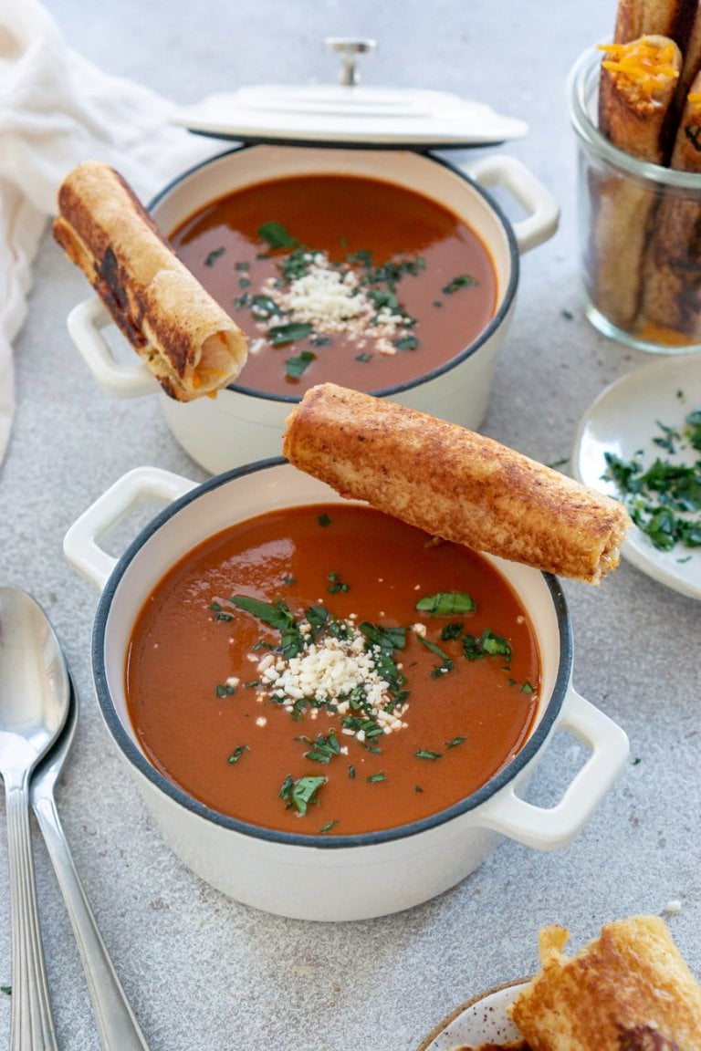 two bowls of tomato soup with grilled cheese roll ups on the edge