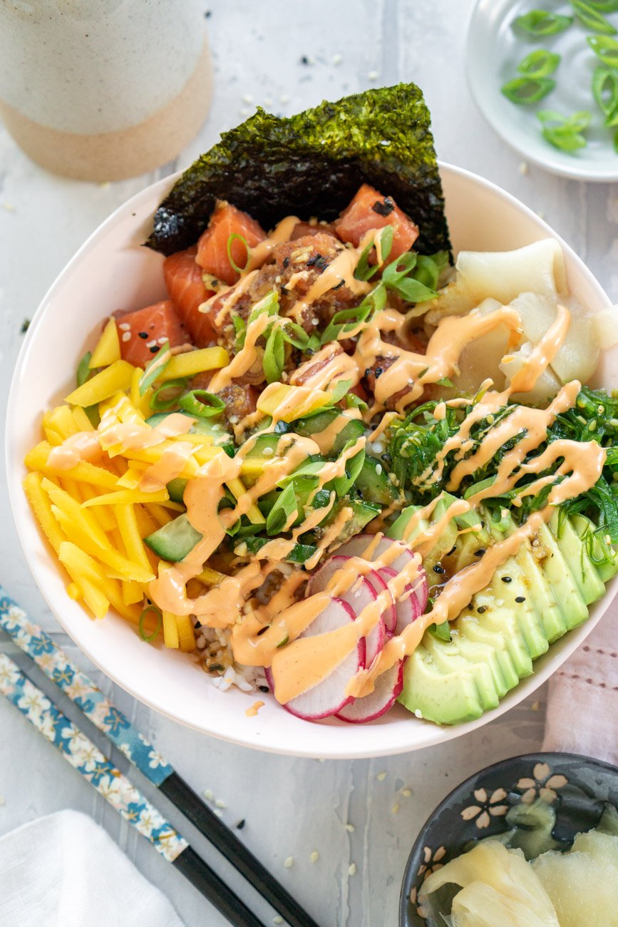 Salmon poke bowl with spicy mayo drizzled on top and chopsticks to the side.