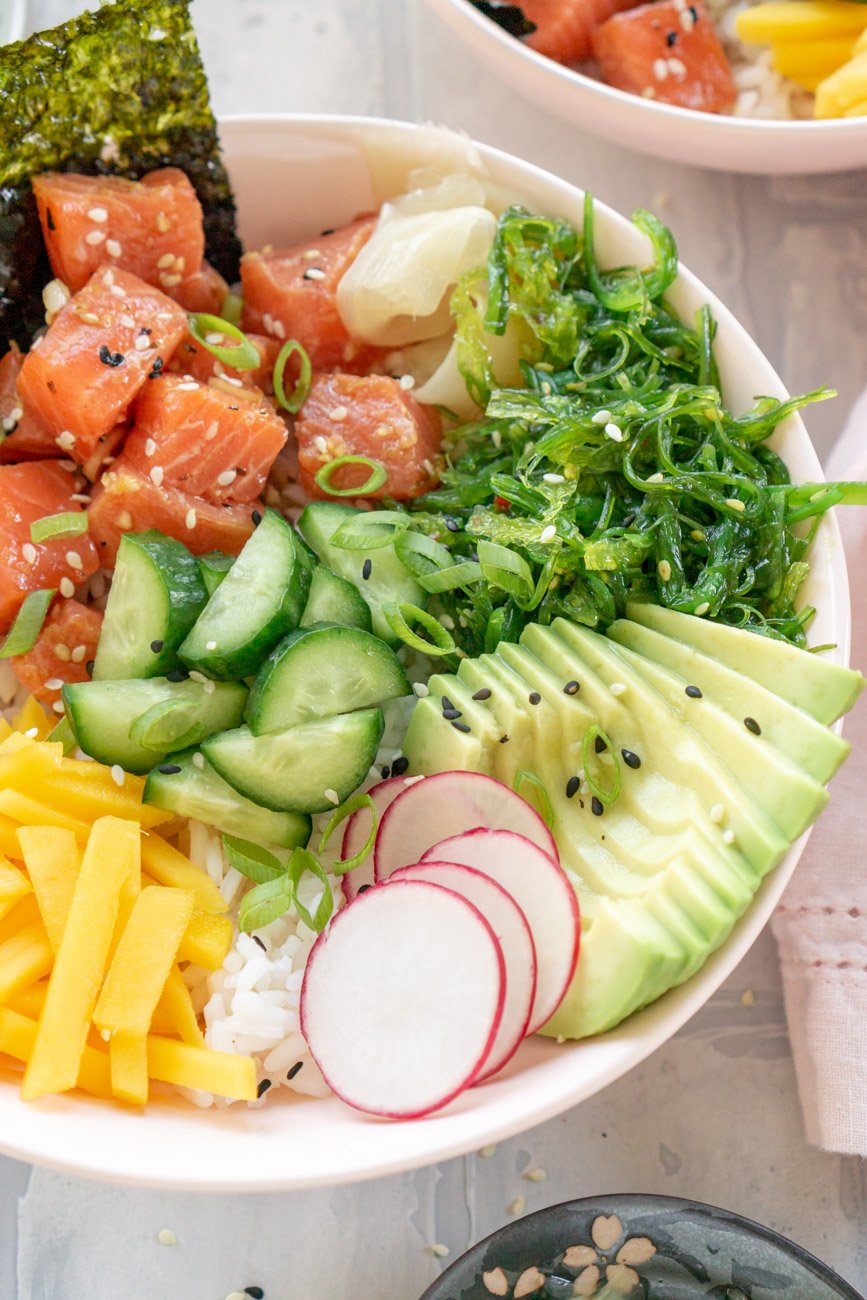 Slose up of a salmon poke bowl with avocado, mango, radish, and seaweed salad.