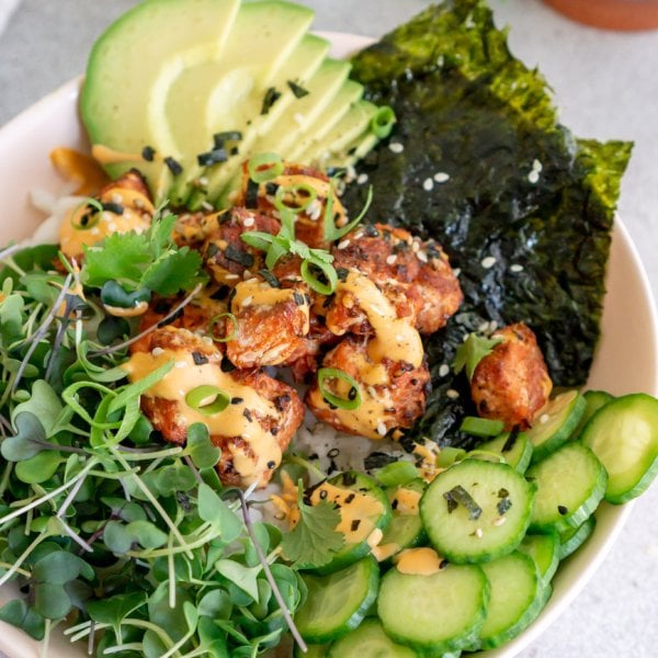 salmon rice bowl with avocado, cilantro, cucumbers, and seaweed paper